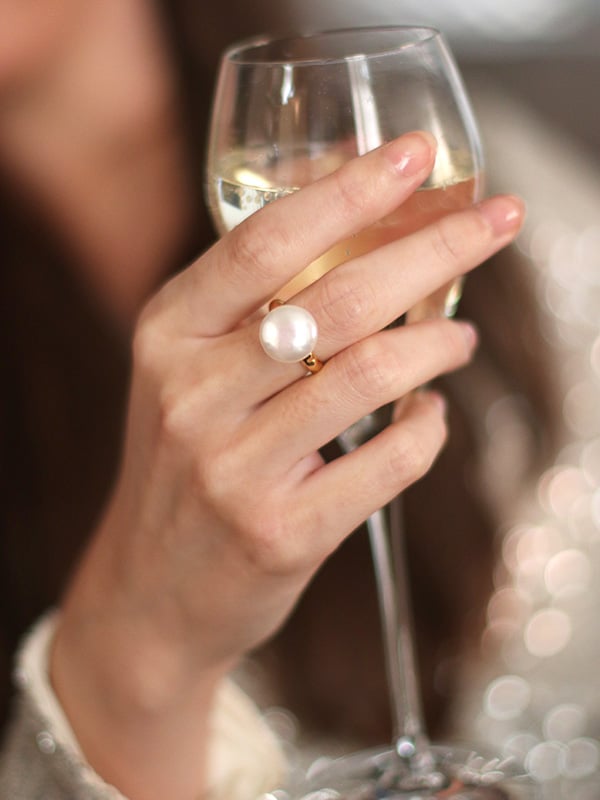 models hand holding a champagne glass with baroque pearl ring on